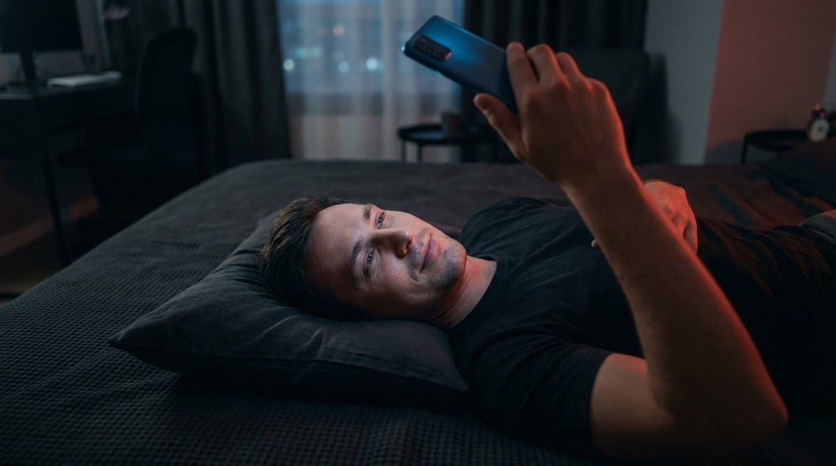 Man lying in bed at night using phone with relaxed expression